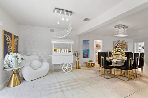 ✨ Luxury Dining & BAR Paradise! Dual crystal chandeliers, elegant dining for 8, sculptural lounge chair & charming bar cart. Butterfly artwork & gold accents create Instagram magic. Hollywood Beach villa with game rooms, hot tub & beach 3min away!