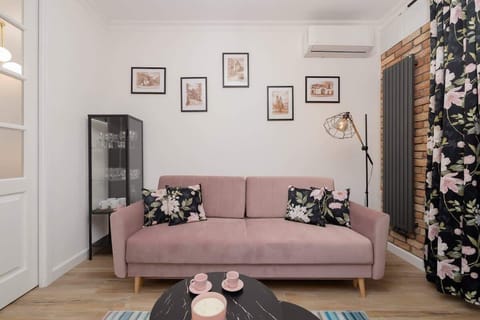 A stylish living room with pink accents, wall art, and a cozy sofa paired with a small black coffee table.