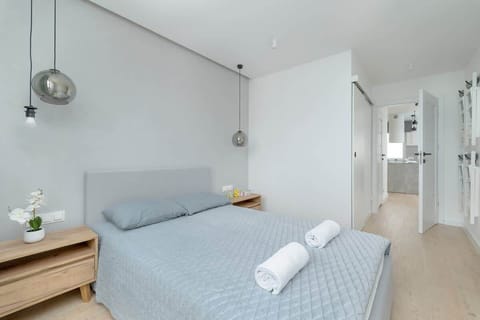 A modern bedroom with a gray upholstered bed, a wooden nightstand, and soft lighting, creating a cozy and minimalist atmosphere.

