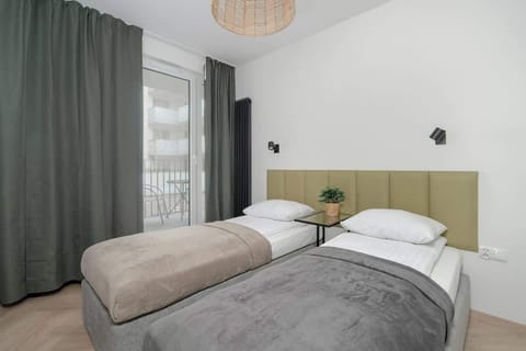 A cosy space with white walls and long curtains. Two single beds with olive-coloured headboard. 