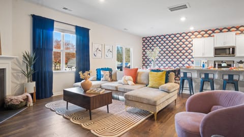 Cozy living area with sectional sofa, patterned accent wall, and a kitchen bar. 