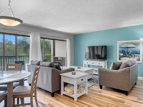 Living room with sofa, chairs, wall-mounted TV, and sliding glass doors to the balcony