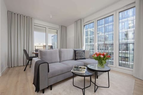 A stylish living room with a gray sofa, a glass coffee table, and floor-to-ceiling windows offering a bright and open atmosphere.

