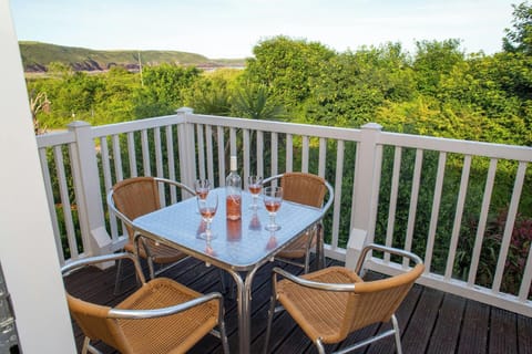 Square outdoor table with four chairs on a wooden deck, with glasses and plates