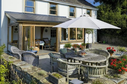 Garden seating area with wooden table, chairs and large parasol outside a two-storey house