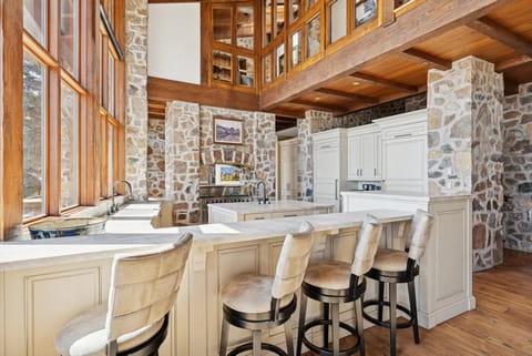 Spacious kitchen with marble countertops, bar stools, and stone walls under wood-beamed ceilings.
