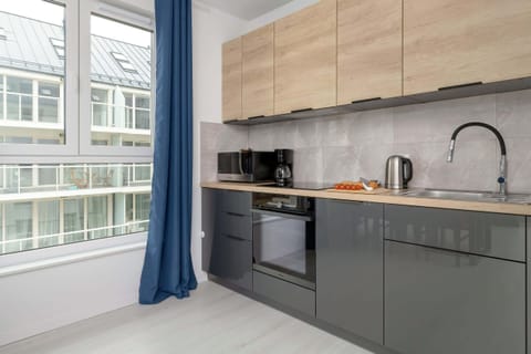 A compact kitchen featuring light wood cabinetry, black countertops, and a large window for natural light.