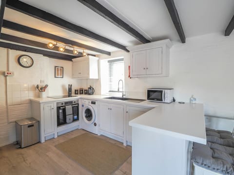 Bright kitchen showing fitted units, cooker, washing machine, sink, microwave, breakfast bar