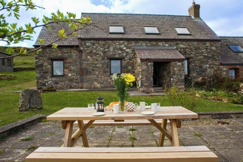 Outdoor picnic table with cups, teapot and flowers outside a stone house