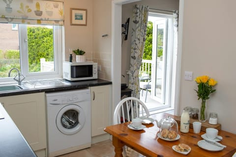 Open plan kitchen/diner: dining table, washing machine, microwave with plant on top and sink under window