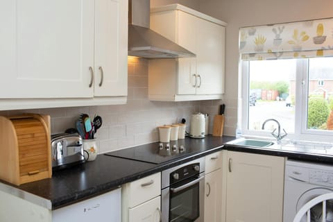 Bread bin, toaster, utensils in a pot, kettle, knives and sugar, tea and coffee pots on worktops