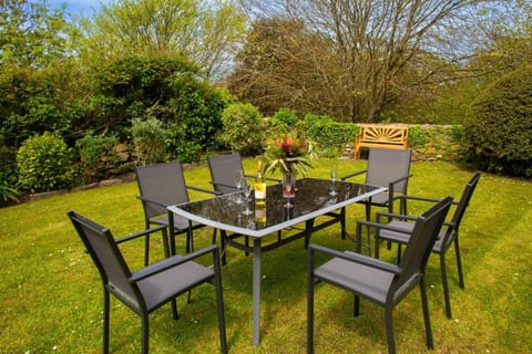 Garden table and 6 chairs surrounded by a lawn and mature flower beds and wooden garden bench
