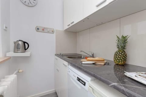 A sleek kitchenette featuring a kettle, a plant, and a pineapple placed on the counter for a fresh touch.

