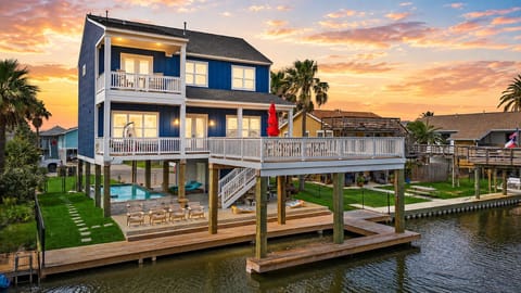 Canal-front Jamaica Beach vacation home with blue exterior, wraparound deck, private dock, outdoor seating, and waterfront views.