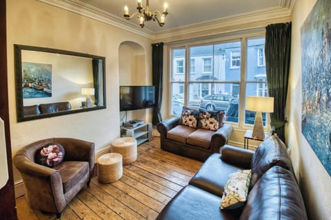 Large window. Wooden floor boards. Two sofas, armchair, large mirror, table with lamp and TV