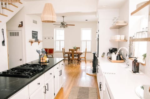 Kitchen overview – Bright and airy chef’s kitchen boasts open shelving, sleek black countertops, and large island, with dining area just beyond 🍳🌿
