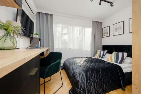 Cozy studio with a bed, desk, green chair, and large window with curtains.