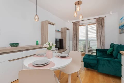 A spacious living room with a TV and bright green sofa. Large windows provide ample daylight and a pleasant view.