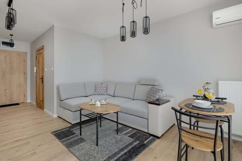 A modern living room with a gray sectional sofa, wooden flooring, and a dining area with pendant lighting.