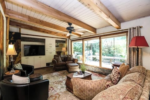 Relax in a spacious yet cozy living room filled with natural light from large picture windows overlooking the outdoors. Enjoy exposed wood beams, plush seating, and a smart TV seamlessly built into custom cabinetry—perfect for unwinding. 