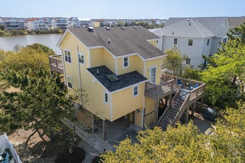 Bright yellow coastal rental home nestled among lush greenery with serene water views, offering spacious decks and a charming neighborhood setting perfect for your beach getaway.