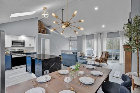 Welcome to Pocono Blue! Stylish open-plan living area featuring a modern kitchen with a large island, dining table set for six, and a comfortable seating area. Highlights include elegant lighting fixtures, natural light from large windows, and a spacious 