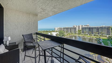 Living room balcony with black metal railing, wicker seating, and lake view extending toward Gulf horizon.
