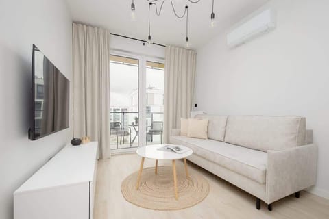A cozy living room with a beige sofa, round coffee table, and a TV area bathed in natural light. Perfect for relaxing or entertaining guests in a bright, modern space.