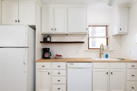 Our modern kitchen boasts white cabinets, wooden countertops, and an array of appliances, emitting a clean and organized atmosphere ideal for culinary exploration.