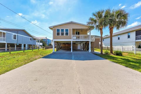 A coastal property on stilts with covered parking and palm trees, situated in a quiet residential neighborhood near the beach.
