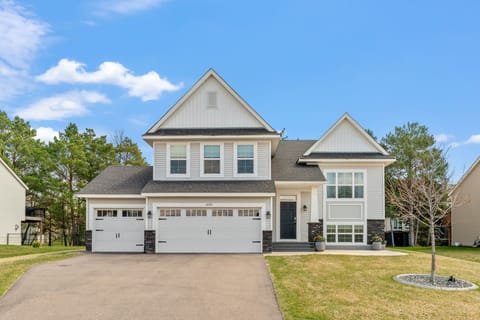 Modern two-story home with white siding, stone accents, and spacious three-car garage in peaceful residential neighborhood.