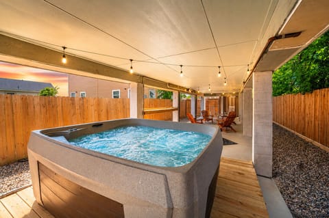 Covered outdoor hot tub retreat with relaxing spa seating, string lights, privacy fencing, and shaded entertainment space in Galveston vacation rental near the beach.