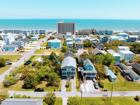 Aerial view of beachfront neighborhood with vacation rental homes nestled among mature trees, just steps from the ocean.