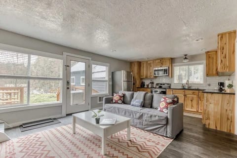 Cozy cabin-style space with wood cabinets, a gray couch, and bright natural light. Opens to a deck with peaceful outdoor views.
