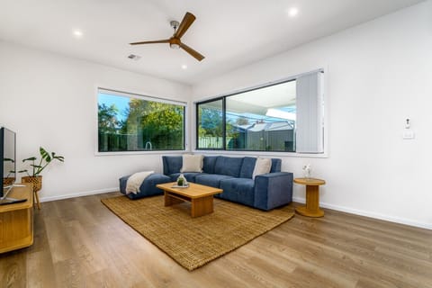 Experience style and sunlight in this inviting Family room, adorned with a cozy Koala blue sectional, expansive windows, and a serene ambiance ideal for unwinding. Next to the living room, find a dining area and modern kitchen, seamlessly integrated.