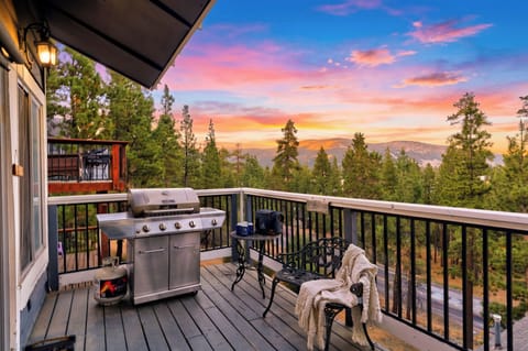 Sunset balcony with a BBQ grill, cozy seating, and sweeping forest and mountain views.