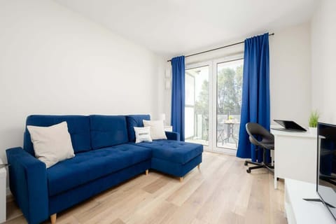 A cozy living area with a blue corner sofa, a small white coffee table, and a large window allowing natural light to brighten the space.