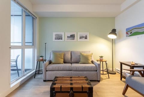 Welcome to your cozy city retreat! Relax in this bright open-concept living room featuring floor-to-ceiling windows and sofa seating.