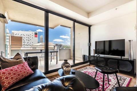 LIVING ROOM: A stylish retreat featuring rich dark tones and natural light from floor-to-ceiling windows. With a smart TV and comfortable seating, it’s the perfect place to relax or entertain.