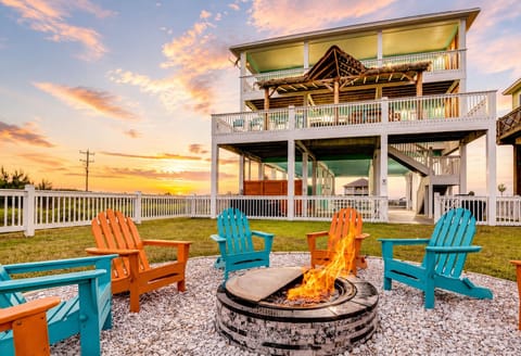 Bolivar Peninsula vacation home with a fenced waterfront yard, colorful Adirondack chairs, stone fire pit and spacious covered decks for relaxed outdoor gatherings.