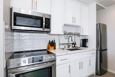 A sleek and modern kitchen featuring stainless steel appliances, white cabinetry, and a glossy subway tile backsplash. This compact yet efficient space is equipped with all essentials, making it perfect for cooking and meal preparation.