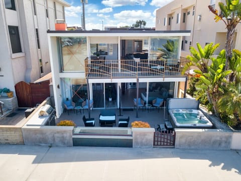 A stunning two-story beachfront home featuring expansive glass windows, multiple outdoor seating areas, and a shared hot tub, offering a perfect blend of luxury and relaxation with breathtaking ocean views.