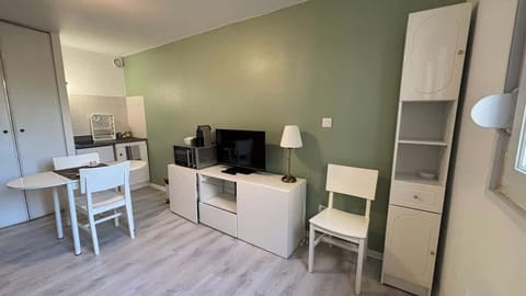 Salon avec canapé convertible et télévision, ouvert sur l'espace de cuisine et séparé de celui-ci par un coin repas pour deux personnes.