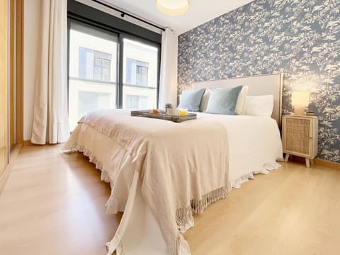Main bedroom that combines a designer wallpaper with a neutral and bright palette. The upholstered headboard and natural fiber nightstands elevate the aesthetic level of the space.