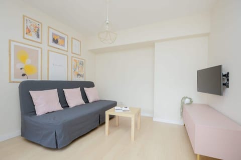 A cozy living room space with a sofa bed, armchair, and TV. Soft lighting and artwork create a welcoming atmosphere.