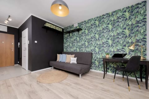 A stylish living room with green botanical wallpaper and wooden flooring. A dining area with dark furniture is tucked into the corner.