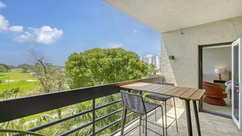 The living room features a rust-orange swivel chair, a floor lamp with a red base, and an open door to the balcony.
