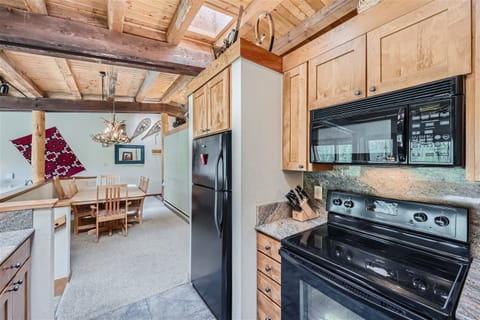 A cozy kitchen with wooden cabinets, black appliances including a fridge and stove, and an adjacent dining area featuring a wooden table, chairs, and rustic decor.
