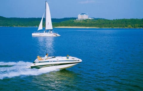 Nearby lake with motorboat speeding across blue water and sailboat gliding near forested shoreline.
