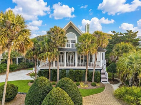 Elegant coastal home with wraparound porches nestled among tropical palms and manicured landscaping under bright blue skies.